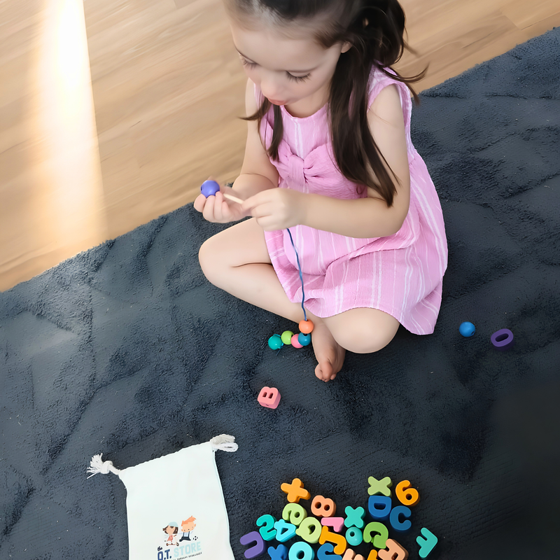 Young girl sitting on a carpet threading colourful alphabet lacing beads for fine motor skills activity