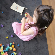Young child sitting on a dark rug threading a green bead onto a string with colorful alphabet beads scattered nearby