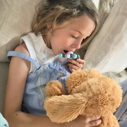 Child wearing a blue and grey pastel chew necklace while cuddling a soft teddy bear