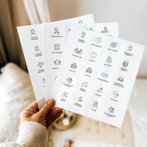Hand holding three sheets of white labels with black line icons and text representing health and support services on a soft neutral background.