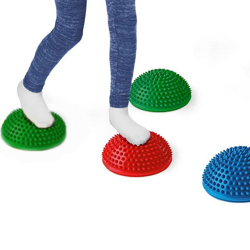 Child wearing white socks stepping on red and green tactile sensory stones with blue stone nearby on white background