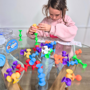 Child playing with colourful suction pop pieces and building patterns on a glass table with educational toys nearby