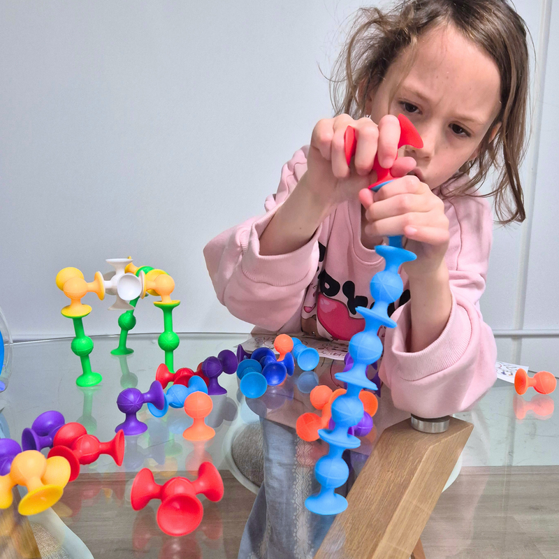 Child playing with colourful suction pieces from an educational toy game on a glass table